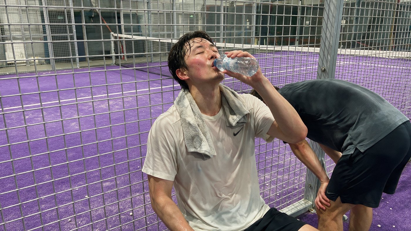 Spieler trinkt nach dem Match am Zaun, lila Court dahinter